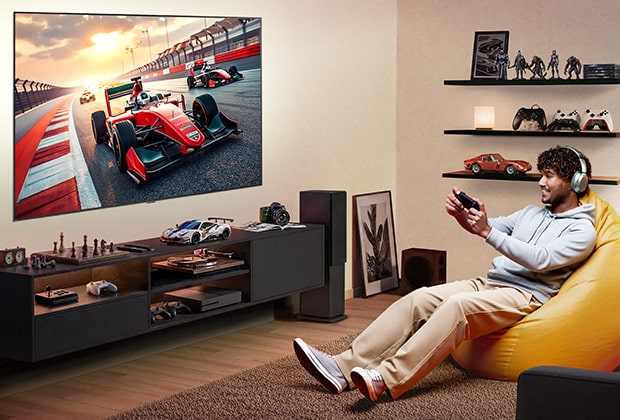 LG TV with big-screen is wall-mounted in a gaming room with gaming gear accents, where a large display shows a high-speed racing scene as a person relaxes on a beanbag, delivering immersive entertainment.