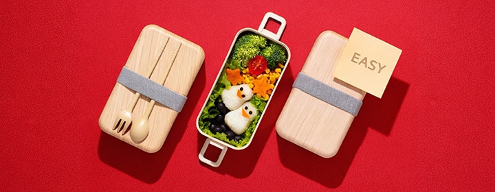 An image showing an easy bento box meal with penguin-shaped rice balls and colorful vegetables on a red background, illustrating a simple meal-prep concept.