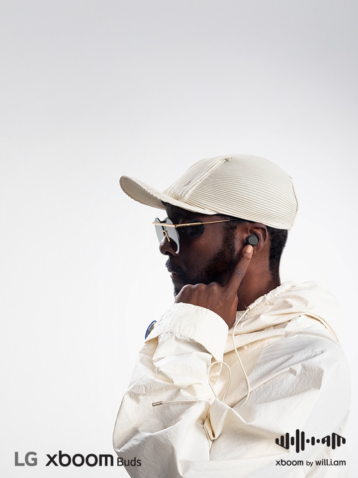 will.i.am in white outfit and sunglasses is his facing right side pointing the earbud in his ear with his left index finger.