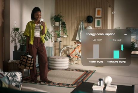 Een video van een vrouw in een geel shirt die glimlachend naar haar telefoon kijkt, met een grafiek die een lager energieverbruik toont.