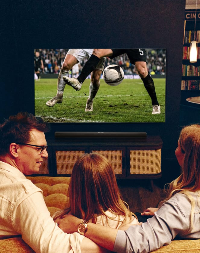 Gezin dat van achteren te zien is terwijl het naar een voetbalwedstrijd op tv kijkt.
