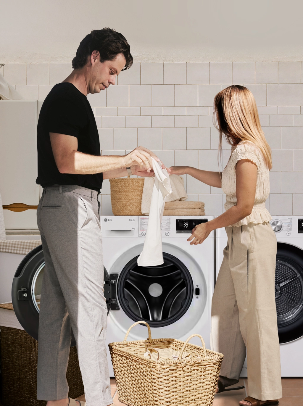 Een man en een vrouw geven witte was door van een LG wasmachine naar een droger in een wasruimte.