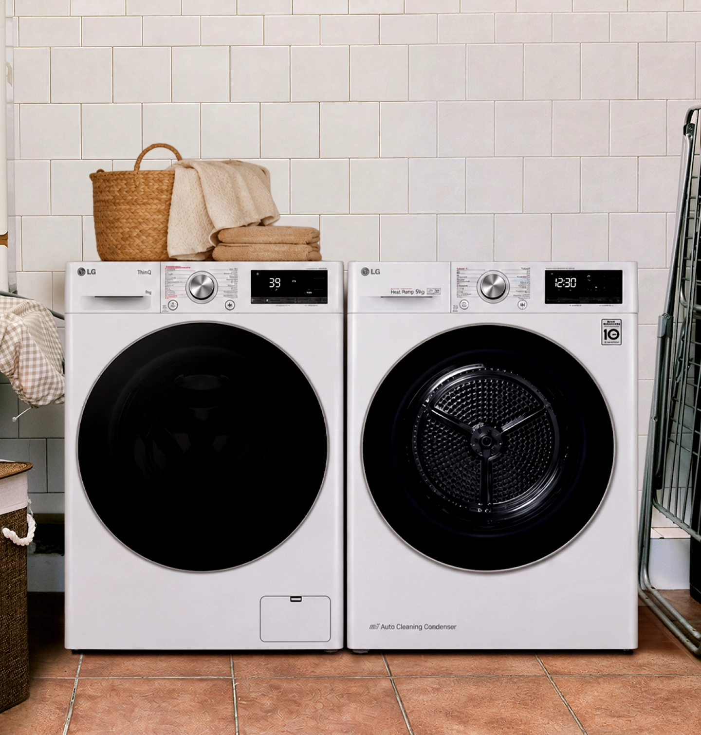 Een witte LG wasmachine en droger in een betegelde wasruimte, met een mand handdoeken erbovenop.