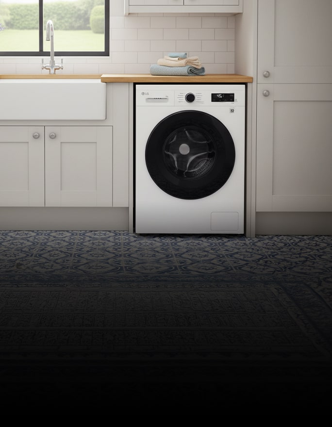 A white front-loading washing machine is placed between white-toned cabinets.