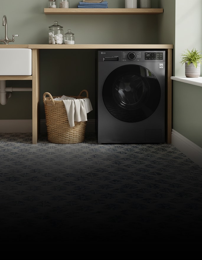 A black front-loading washing machine stands beside wood cabinets, with folded towels on a nearby rack.