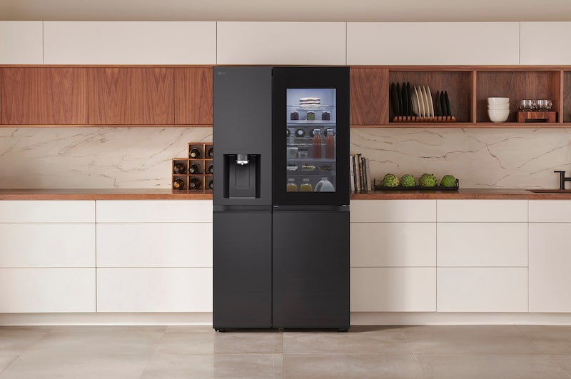 LG Side-by-Side Koelkast GSXE90EVDD in een matzwarte stalen afwerking, naadloos geïntegreerd in een moderne keuken met witte en houten kasten en een waterdispenser.