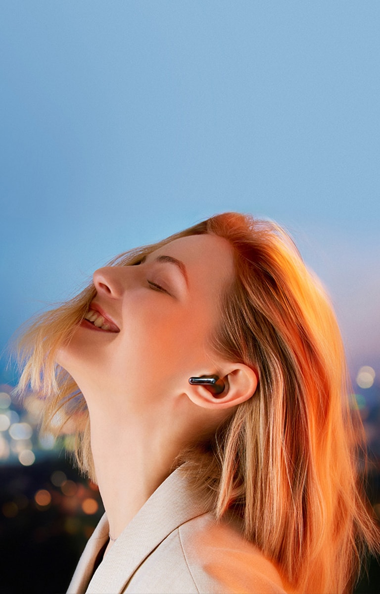 Achter de zin &quot;Refresh Your Listening&quot;, een vrouw die TONE Free draagt tegen de achtergrond van het nachtelijk uitzicht van de stad.