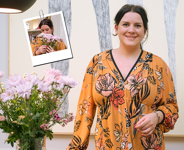 Het is een foto van een vrouw die recht vooruit kijkt, naast een roze bloem	