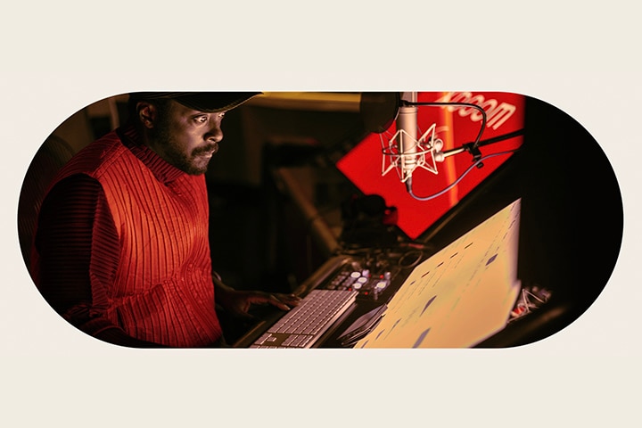 will.i.am is working in studio looking at a screen placed below a mic.	