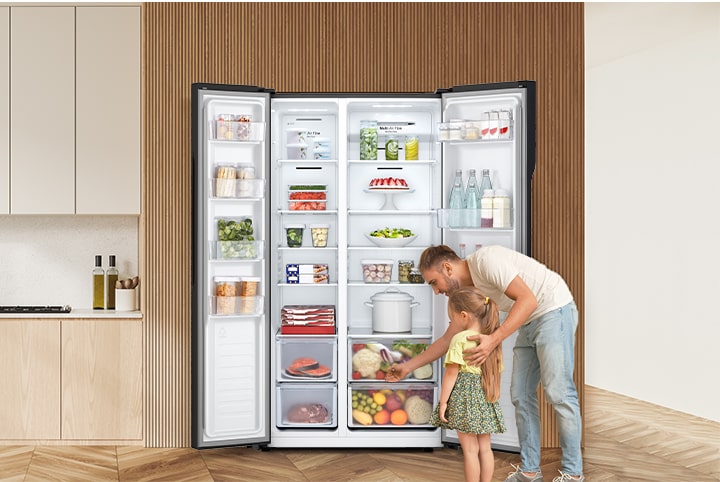 A man and a child are taking out things in front of the refrigerator with the door open