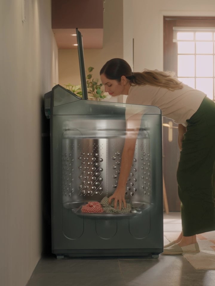 Woman unloading laundry from a top-load washer with a tilted drum structure for easier reach and access
