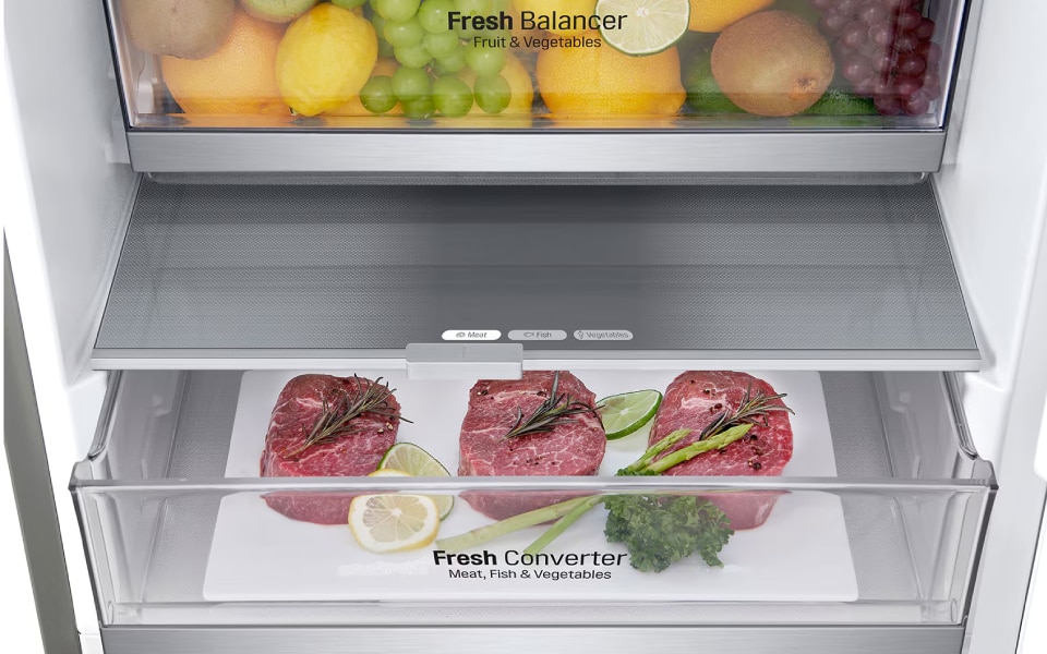 Interior of an LG fridge with two clear drawers. The top drawer is labelled "Fresh Balancer" and filled with various fruits like lemons, grapes, and kiwis. The bottom drawer is labelled "Fresh Converter" contains neatly arranged raw steaks garnished with herbs. The sleek design emphasises organised, fresh storage for various foods.