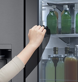 The front view of a black glass InstaView refrigerator with the light on inside. Hands knocking on InstaView screen.