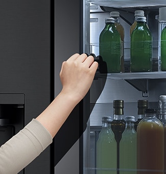  The front view of a black glass InstaView refrigerator with the light on inside. Hands knocking on InstaView screen.