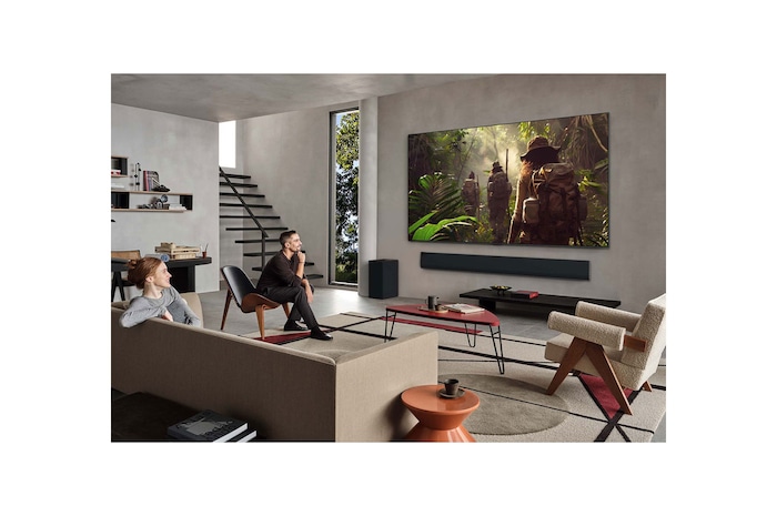 Wide view of a living room inside a premium home, a man is watching a movie on his wall-mounted LG OLED TV. The TV's design blends elegantly with the wall and the interior design.
