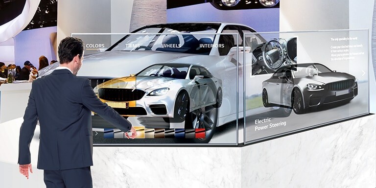 En una sala de exhibición de automóviles, un hombre está cambiando el color del automóvil en la pantalla al tocar la pantalla de señalización OLED transparente instalada frente al automóvil.
