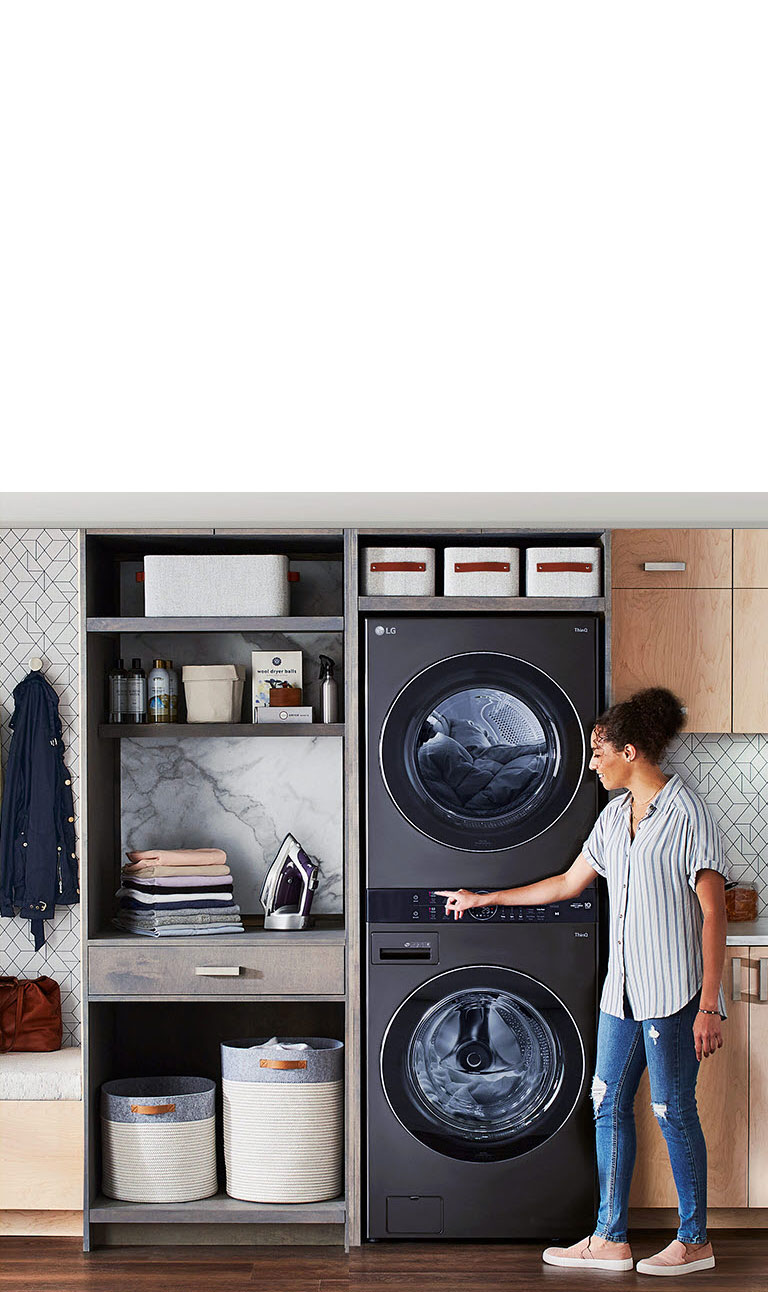 Una torre de lavado LG negra está instalada en un lavadero y una mujer se para a un lado inclinada para presionar un botón en la máquina.