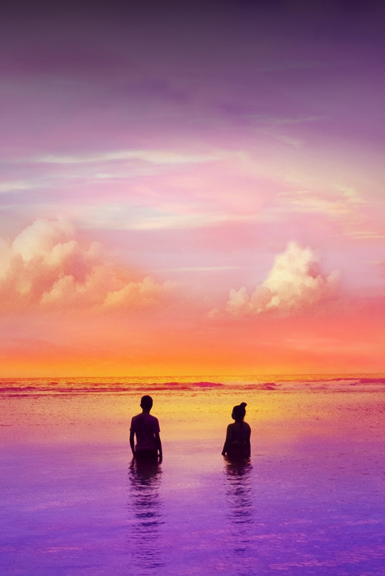 Hay dos personas paradas dentro de un océano en tono morado. Se está poniendo el sol.