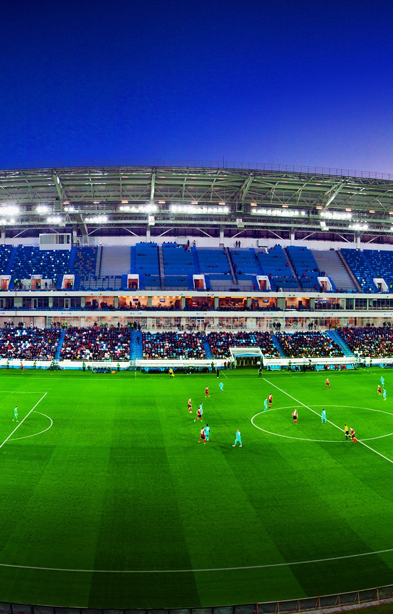 Una toma panorámica de un estadio de fútbol lleno de público y con el partido en progreso.