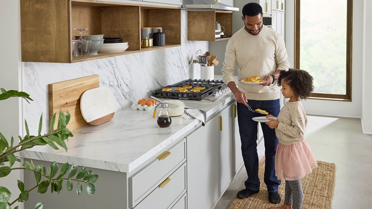 La imágen de un padre y su hija poniendo en un bol la comida cocinada en la cocina.