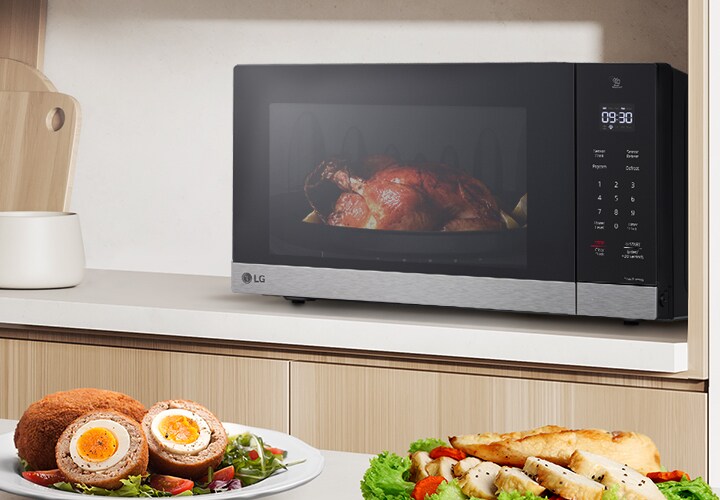 La imagen muestra una variedad de alimentos en la mesa de la cocina, y un pollo rostizado está siendo cocinado por el microondas NeoChef.