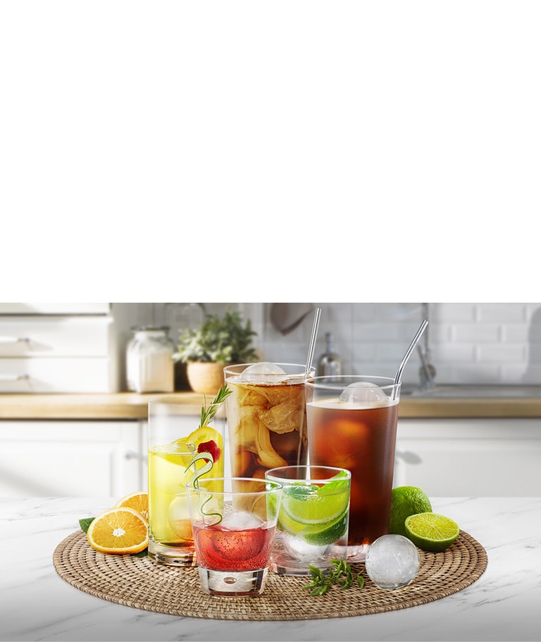 Varios vasos de distintos tamaños que contienen diferentes bebidas con cubitos de hielo redondos están sobre una encimera de cocina.