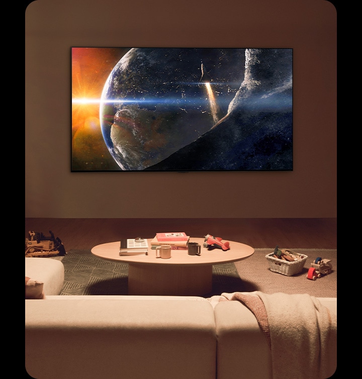Una familia sentada en el suelo de una sala de estar poco iluminada frente a una mesa pequeña mirando un LG TV montado en la pared que muestra la Tierra desde el espacio.