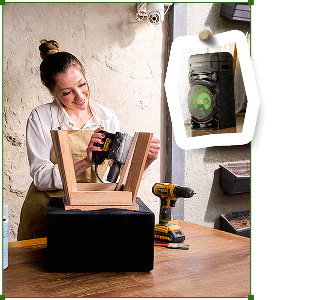 Carol reparando una silla de madera en su mesa de trabajo, con un parlante LG XBOOM.