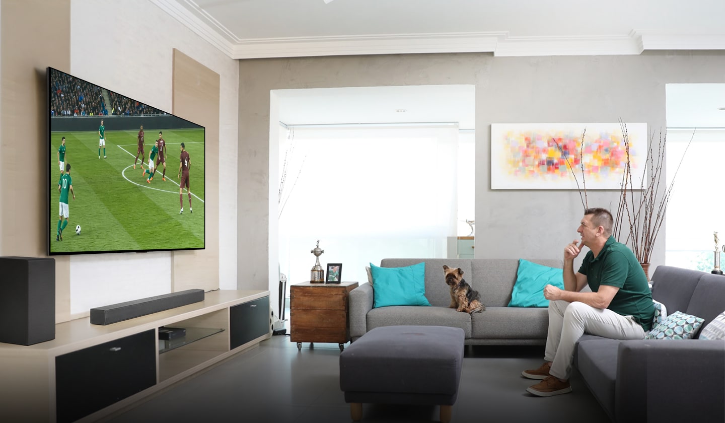 Marcos, sentado cómodamente en el sofá de su sala, observa con interés y analiza un partido de fútbol en su televisor LG de gran tamaño.