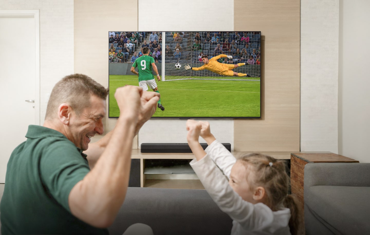 Una familia celebra mientras ve un partido de fútbol, con una barra de sonido y un subwoofer debajo de la TV.