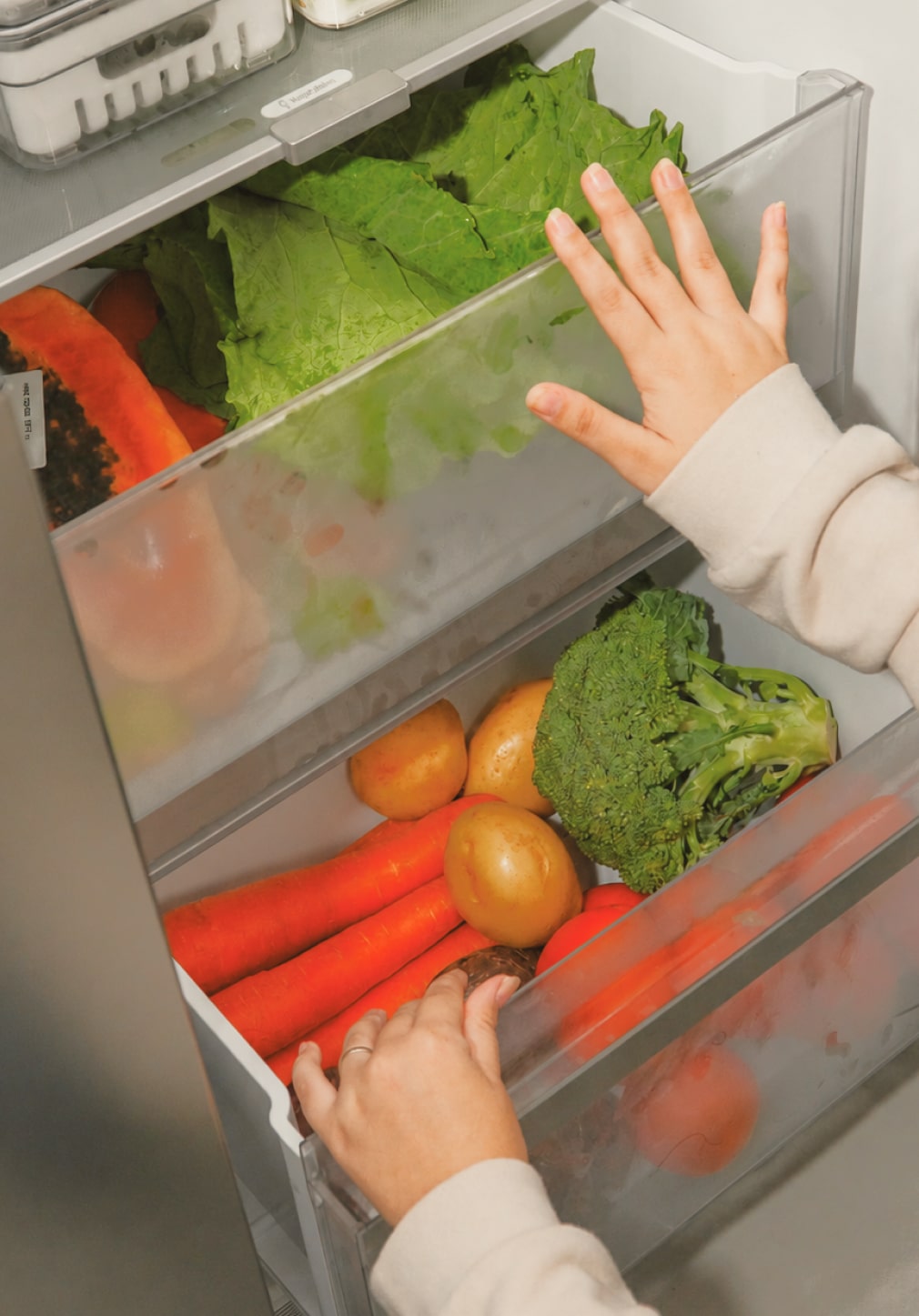 Una mamá saca verduras de hoja y una papa de los cajones para frutas y verduras de la nevera.