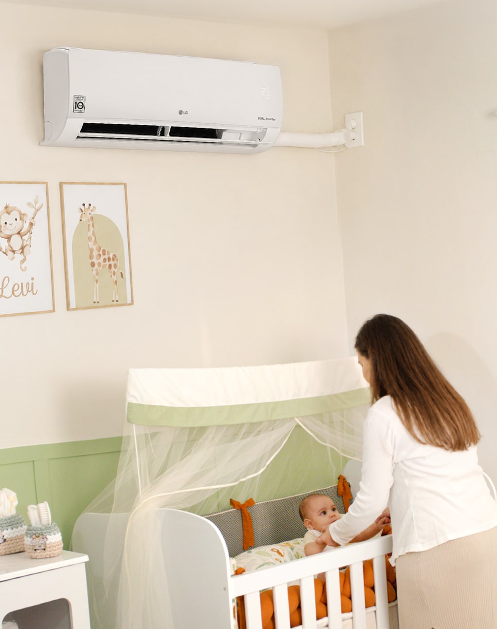 Una mamá toca las manos de su bebé en la cuna, bajo un aire acondicionado LG de pared.