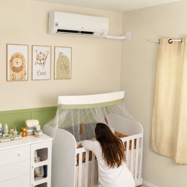 Una mamá se inclina sobre la cuna en la habitación del bebé, bajo un aire acondicionado LG de pared.