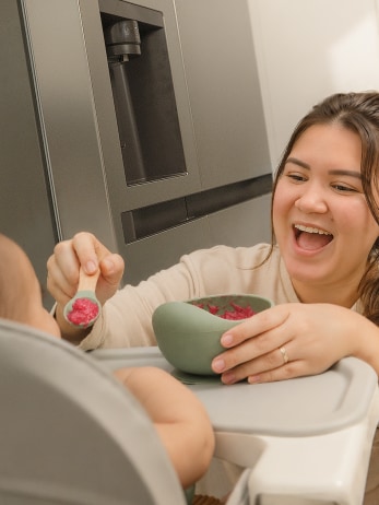 Una mamá alimenta a su bebé con papilla mientras está sentado en su silla alta, en la cocina.