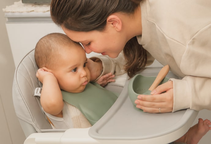Una mamá junta su frente con la de su bebé, que está sentado en una silla alta.
