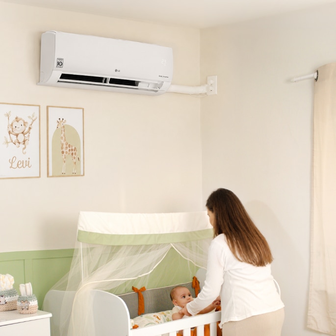 Una mamá toca las manos de su bebé en la cuna, bajo un aire acondicionado LG de pared.