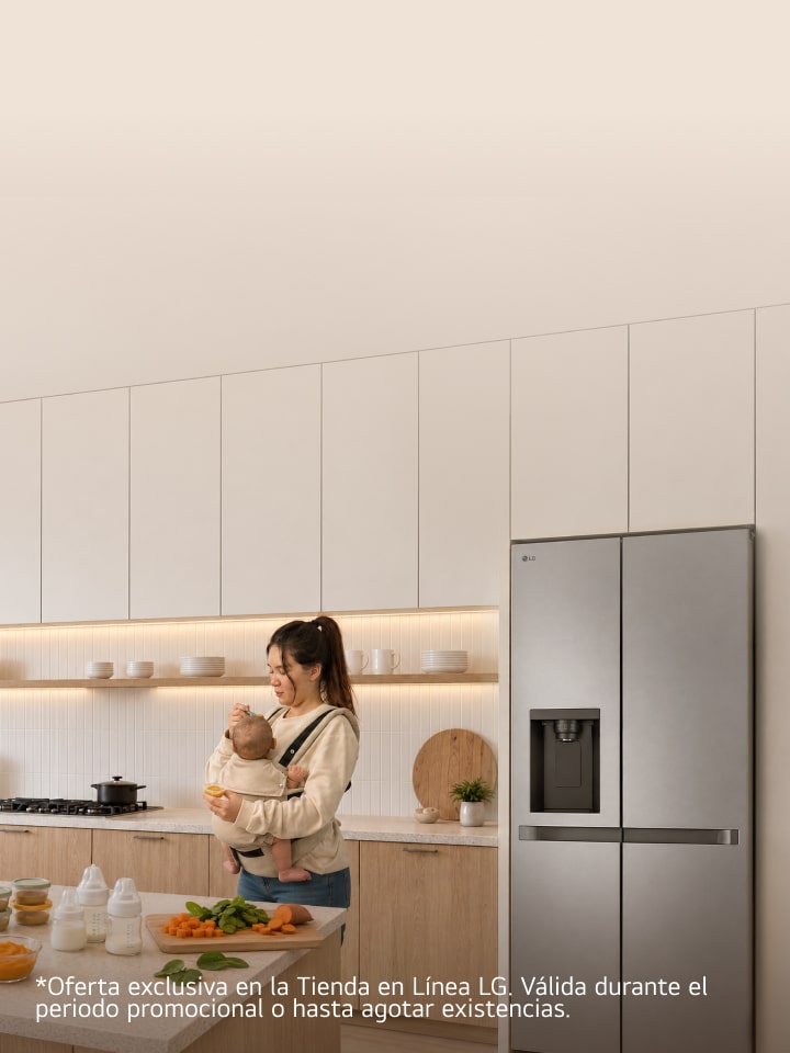Una madre sostiene a su bebé mientras prepara alimentos en una cocina moderna, con una refrigeradora LG de puertas francesas al fondo.