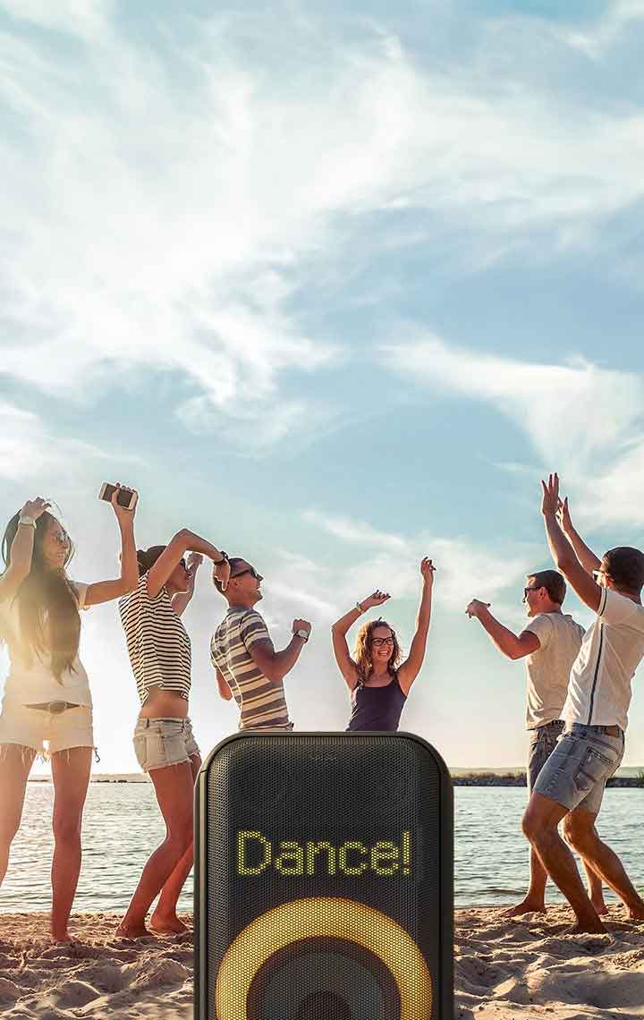Primer plano de píxeles con el texto '¡Baila!'. Abajo, anillo naranja encendido. Detrás, gente baila en la playa.