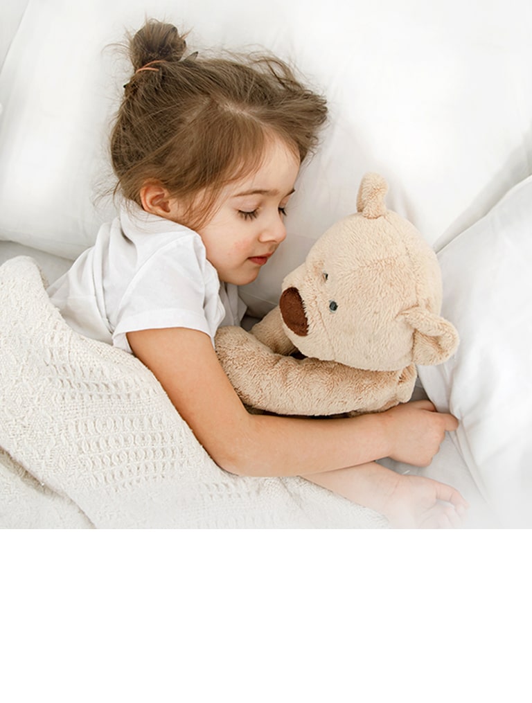 Una niña está tumbada en la cama con una muñeca en brazos
