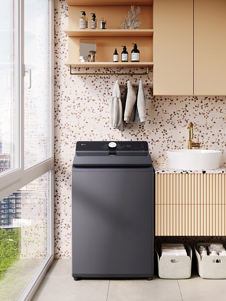 Lavadora de carga superior LG gris oscuro en un lavadero luminoso con plantas, cestas de almacenamiento y vista de la ciudad a través de las ventanas