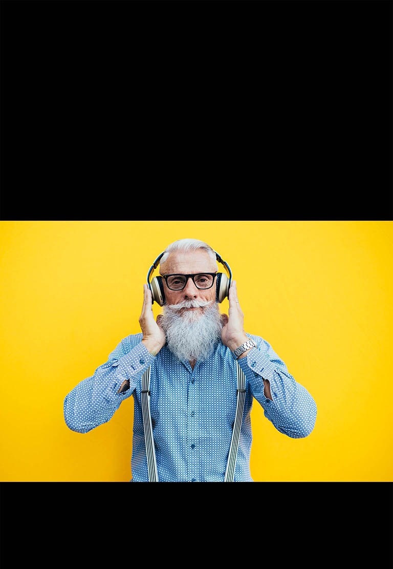 Un abuelo está parado frente a una pared amarilla, con auriculares.