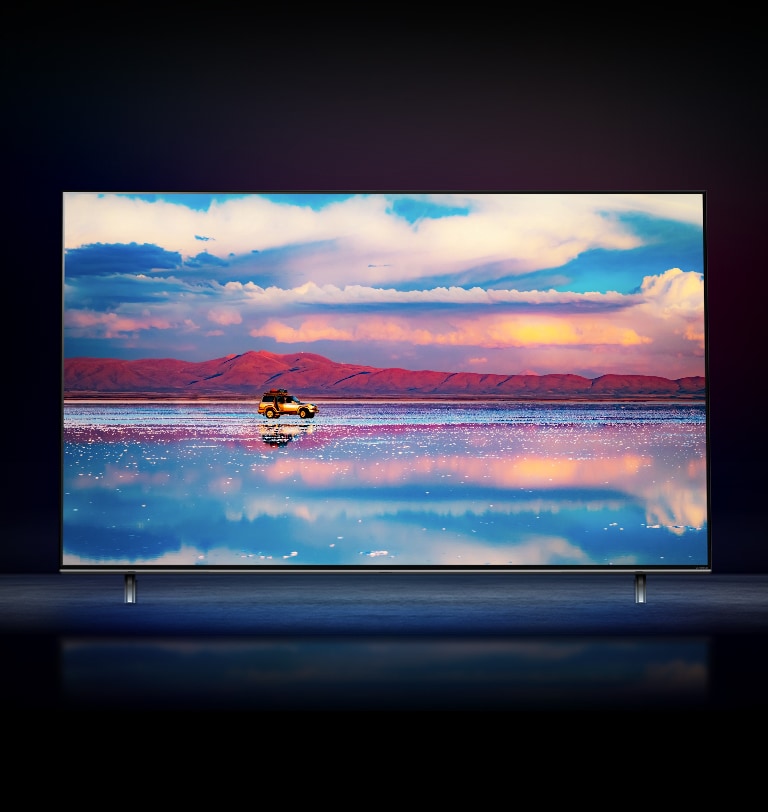 Un televisor LG NanoCell sobre un fondo negro. El televisor muestra un automóvil que pasa frente a una cadena montañosa baja y un espejo de agua que refleja el cielo intenso.