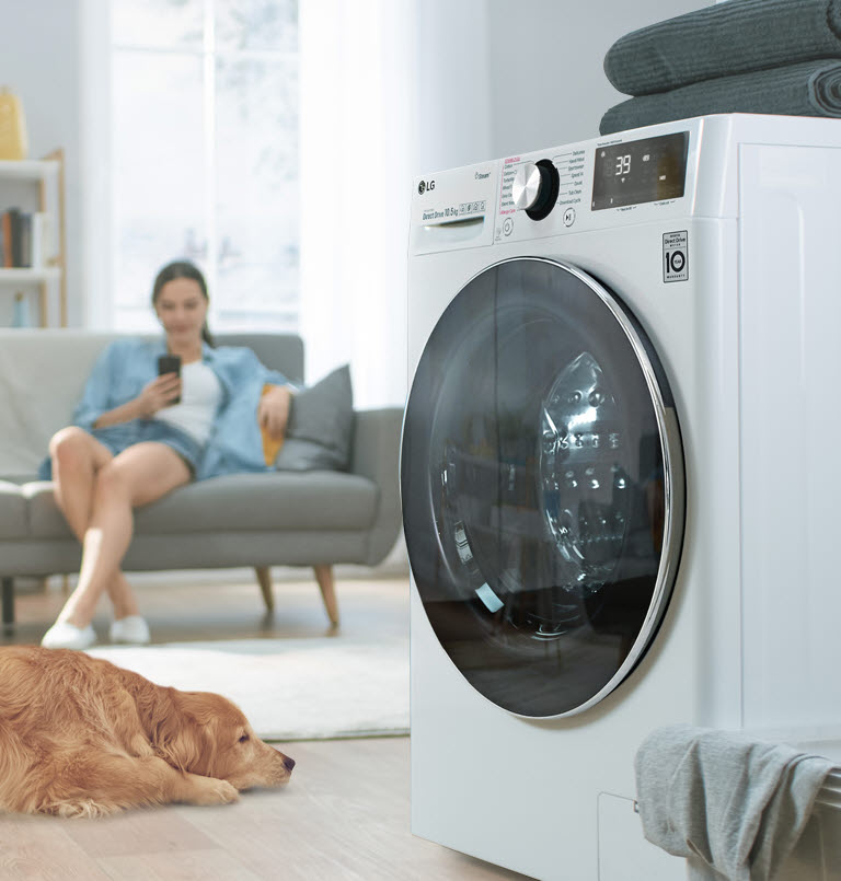 Una vista lateral de la lavadora ubicada a un lado con un perro y una mujer en su teléfono al otro lado.