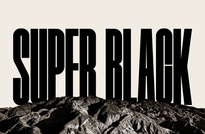 Las palabras "SUPER BLACK" aparecen en negrita y en mayúsculas negras. A continuación, una escena montañosa negra de nítida definición se eleva para cubrir las letras, revelando también un pueblo y dunas de arena. El texto negro desaparece tras un cielo negro.