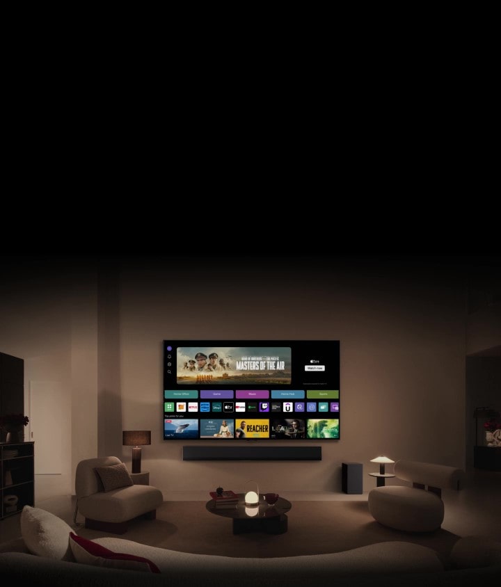 Un primer plano de la pantalla del TV LG muestra los botones Home Office, Game y Music sobre un banner de Masters of the Air, se aleja para mostrar el televisor montado en la pared de un salón. En la imagen aparecen los siguientes logotipos en la pantalla : LG Channels, Netflix, Prime Video, Disney TV, Apple TV, YouTube, Spotify, Twitch, GeForce Now y Udemy.