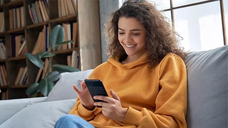 Una mujer mira su teléfono móvil mientras utiliza la aplicación LG ThinQ para controlar a distancia su refrigeradora LG.