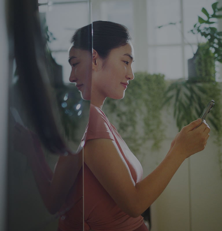 La imagen muestra a una mujer de pie junto a una torre de lavado LG WashTower™, mirando su teléfono mientras sonríe.