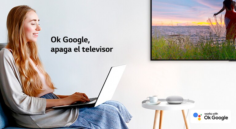 Una mujer sentada en un sofá con un portátil en una habitación con un televisor en la pared ordena a un altavoz de IA que apague el televisor.