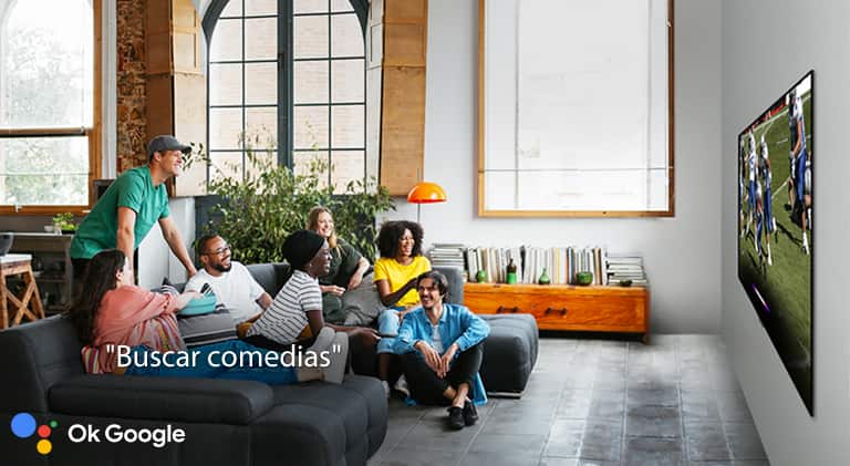 Mujer viendo el fútbol en la televisión con amigos y pidiendo al Asistente de Google que busque comedias.