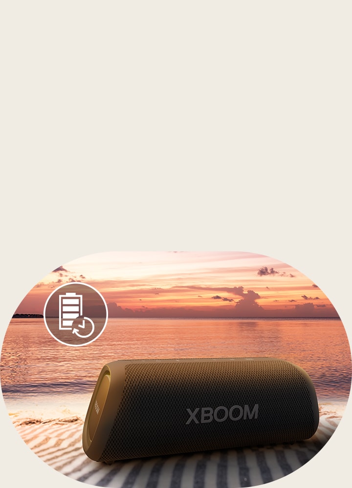 Parlante LG XBOOM sobre una manta en la playa al atardecer, con icono de batería en la esquina superior izquierda.